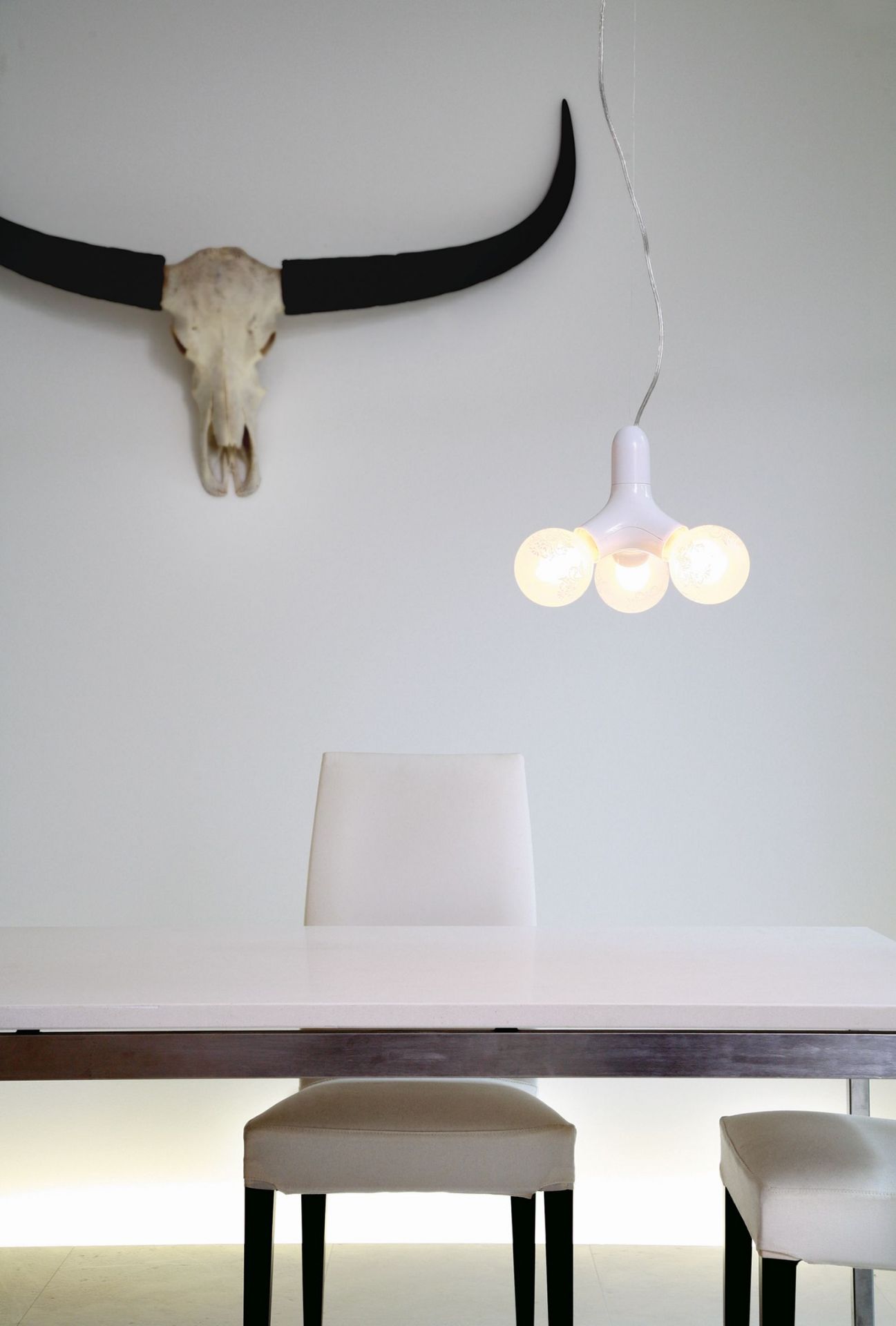 Moderne DNA Pendelleuchte mit drei Leuchten in Kupfer über Esstisch und Stühlen.