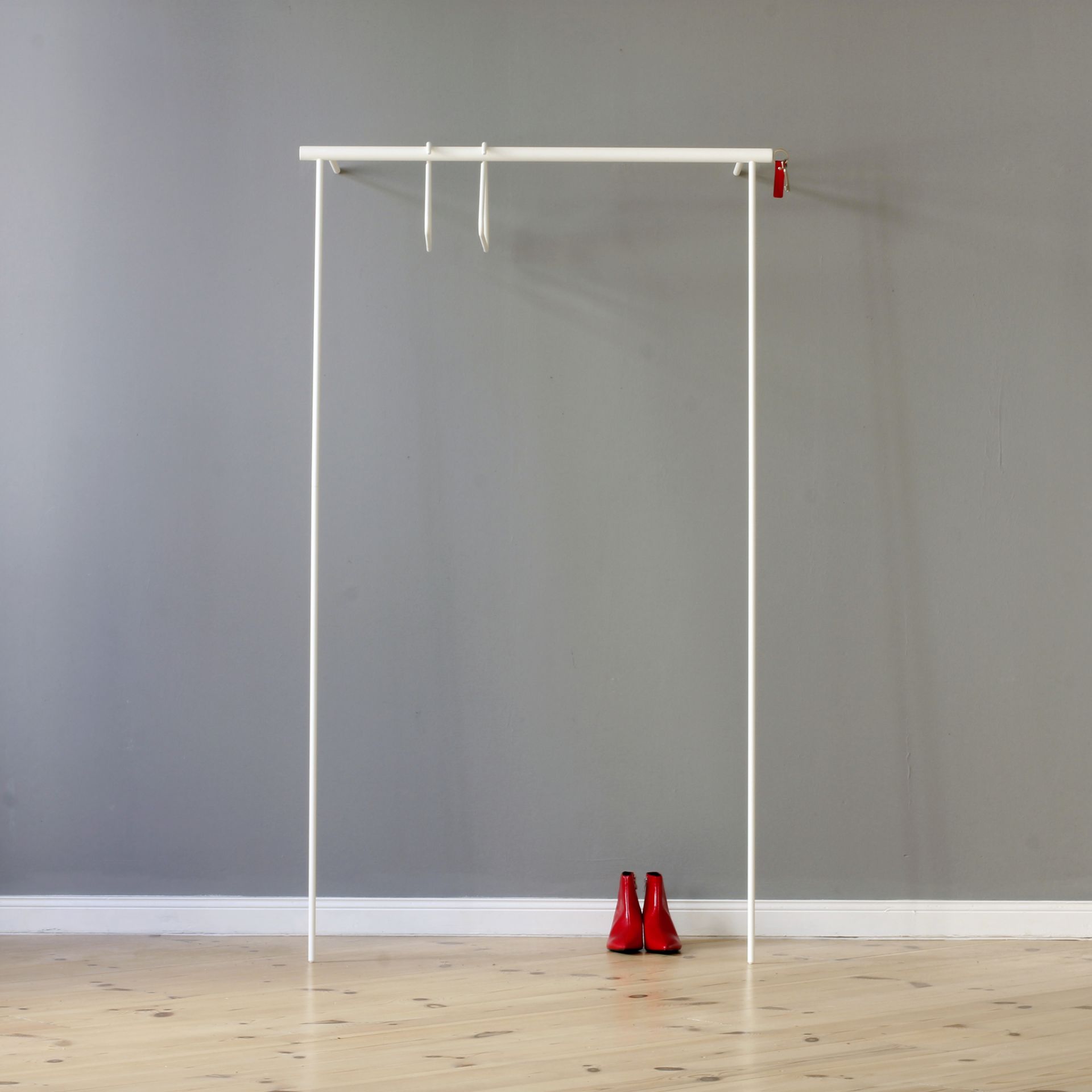 Weiße Leanon II Anlehngarderobe von Roomsafari mit roten Schuhen davor, minimalistisches Design für Flur und Schlafzimmer.