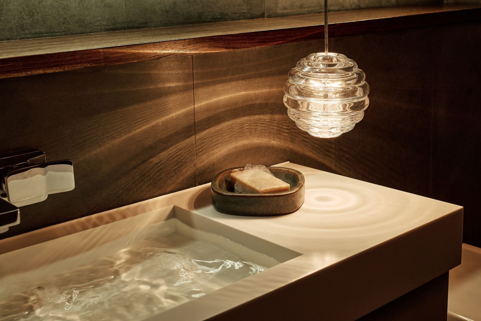 Nahaufnahme: Press Mini Pendelleuchte von Tom Dixon über einem modernen Waschbecken mit Wasser.