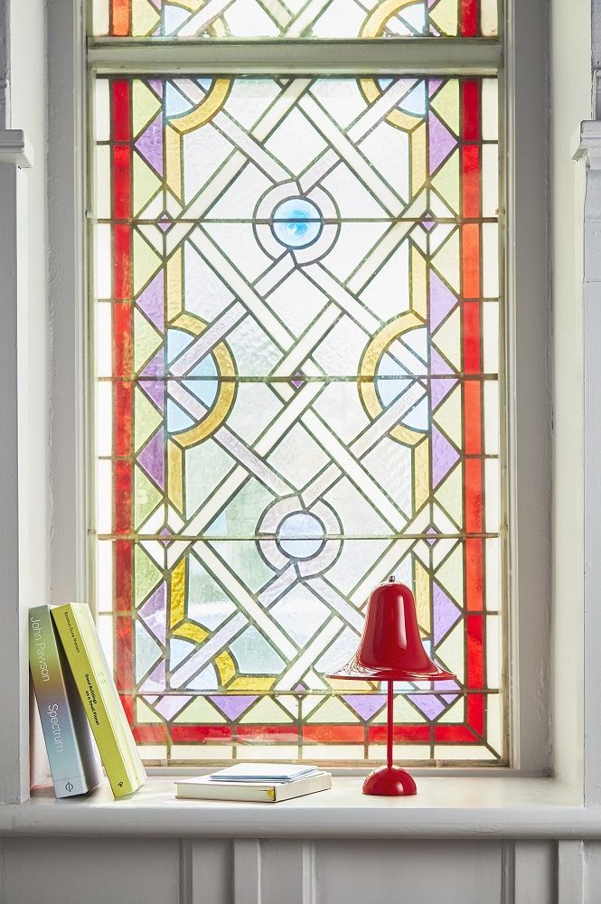 Rote Pantop Tischleuchte von Verpan auf einer Fensterbank mit Buntglasfenster im Hintergrund.