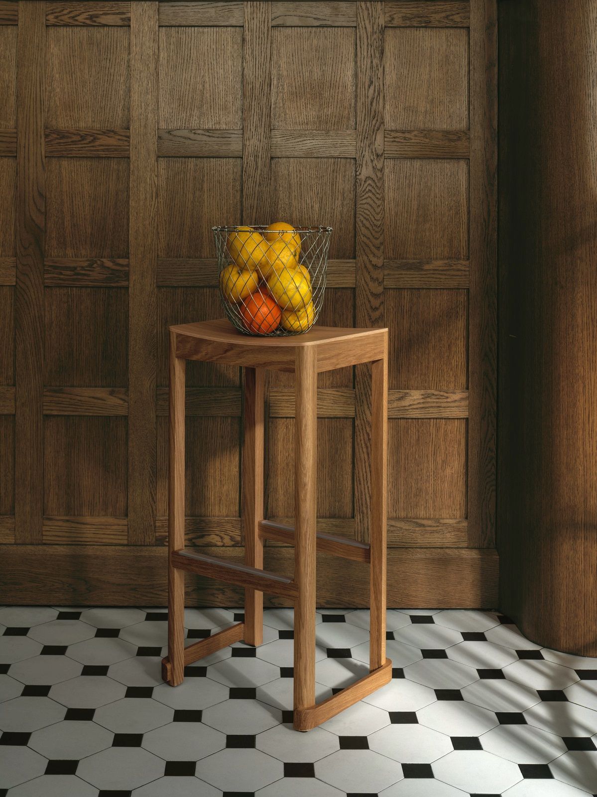 Atelier Bar Stool Barhocker Artek aus Holz mit Obstkorb vor Holzwand.