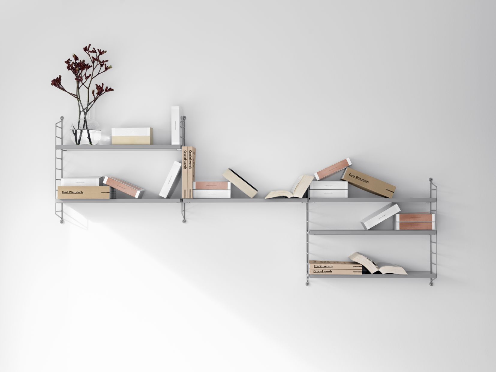 Graue String Furniture Wandleiter mit Regalböden, dekoriert mit Büchern und einer Vase mit Blumen.