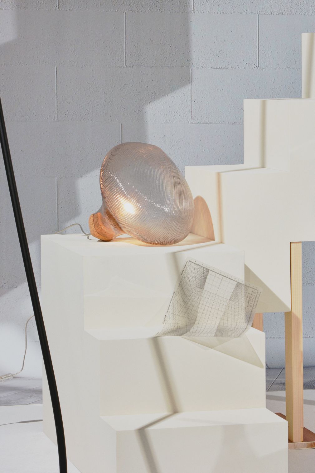 Tidelight Tischleuchte von Petite Friture, moderne Lampe mit geripptem Glasschirm und Holzfuß auf weißem Podest.