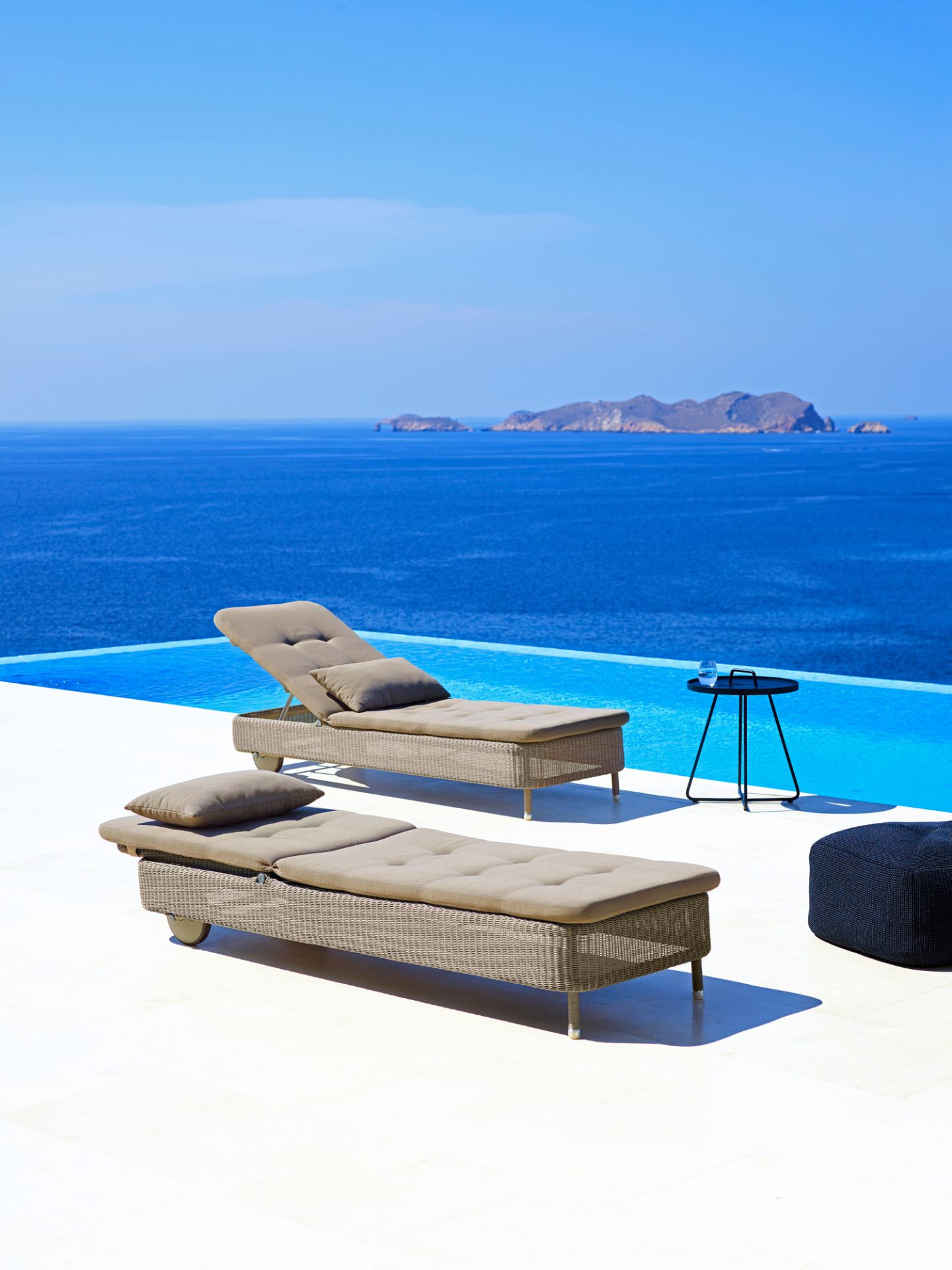 Zwei Cane-Line Sonnenliegen in Taupe am Pool mit Meerblick. Outdoor Liegen aus Rattan.