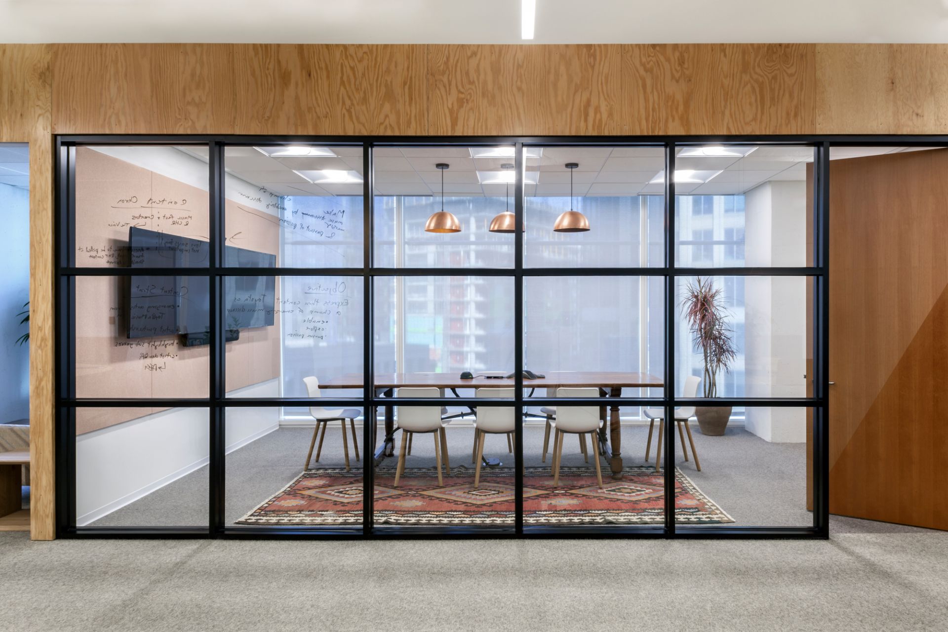 Konferenzraum mit Holztisch, Teppich und weißen Stühlen, möglicherweise Vitra Hal Ply Wood Stühle.