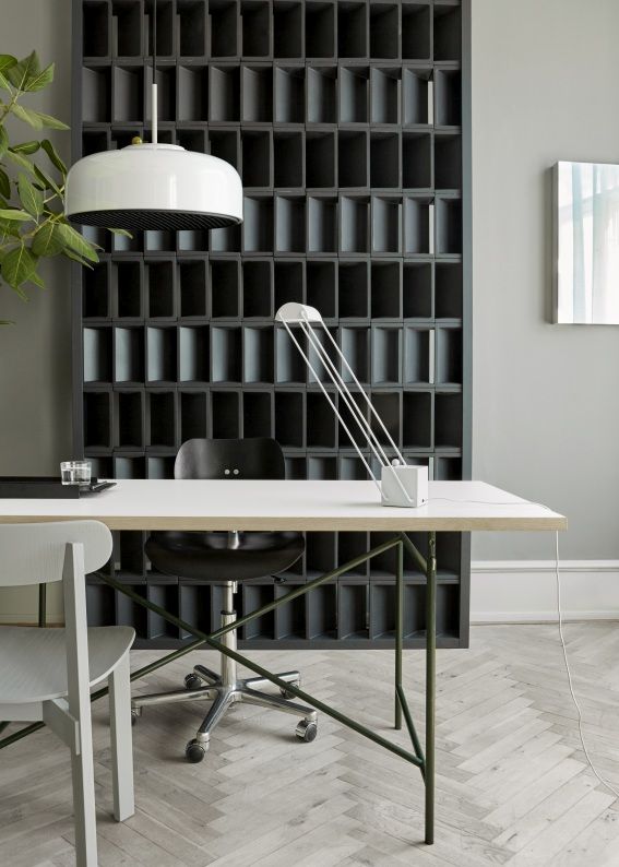 Moderner Schreibtisch mit weißer Tischplatte, grünen Beinen und weißer Lampe vor einem dunklen Regal.