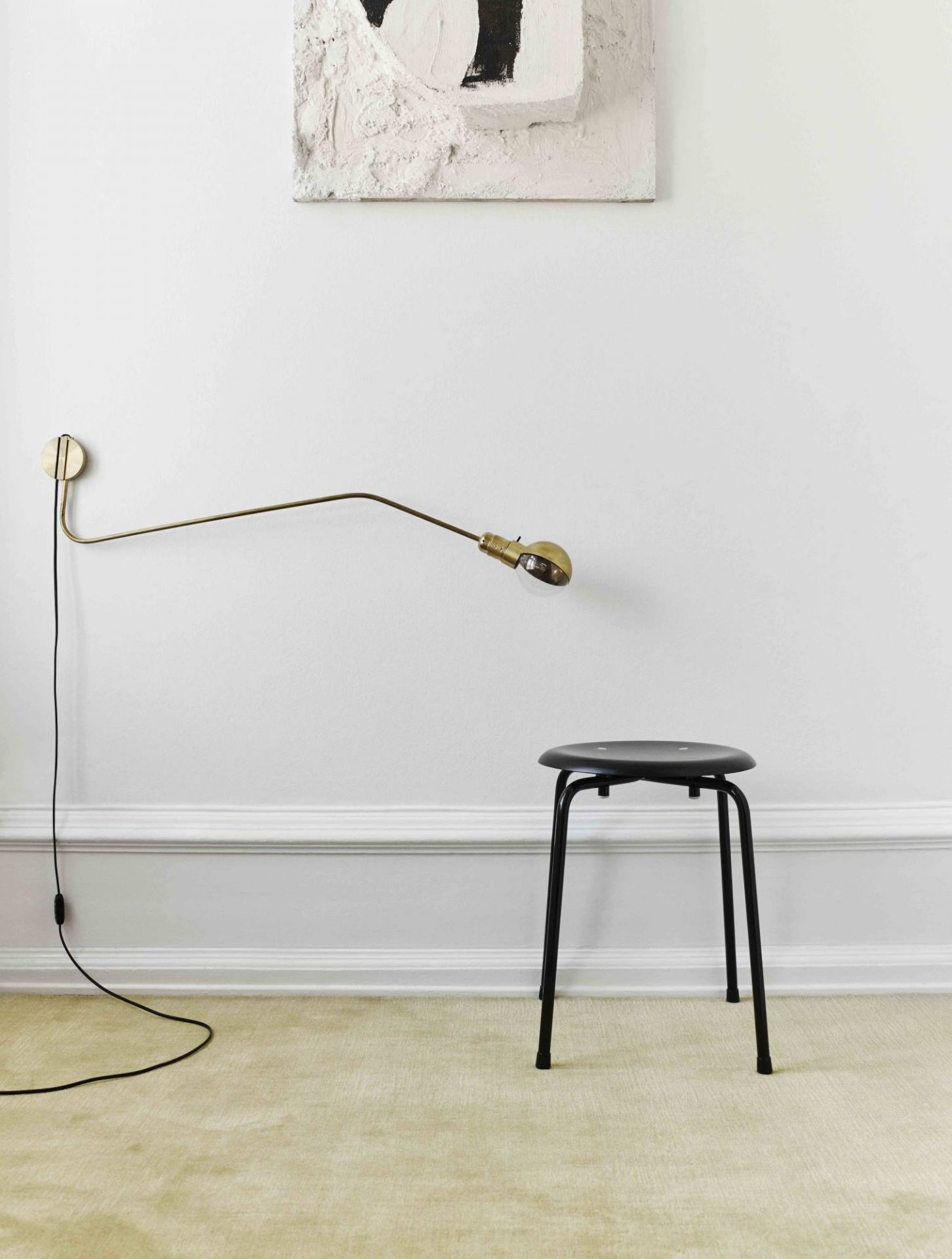 Schwarzer S 38 Hocker von Wilde+Spieth vor weißer Wand mit Lampe und Kunstwerk.