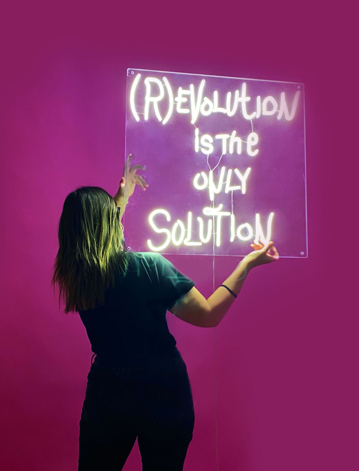 Frau befestigt Revolution LED Wandleuchte von Seletti an pinker Wand. Dekorative Neon-Leuchte.
