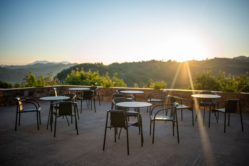 Nami Armrest Dining Chair Outdoor Houe: Mehrere schwarze Armlehnstühle mit Tischen auf einer Terrasse bei Sonnenaufgang.