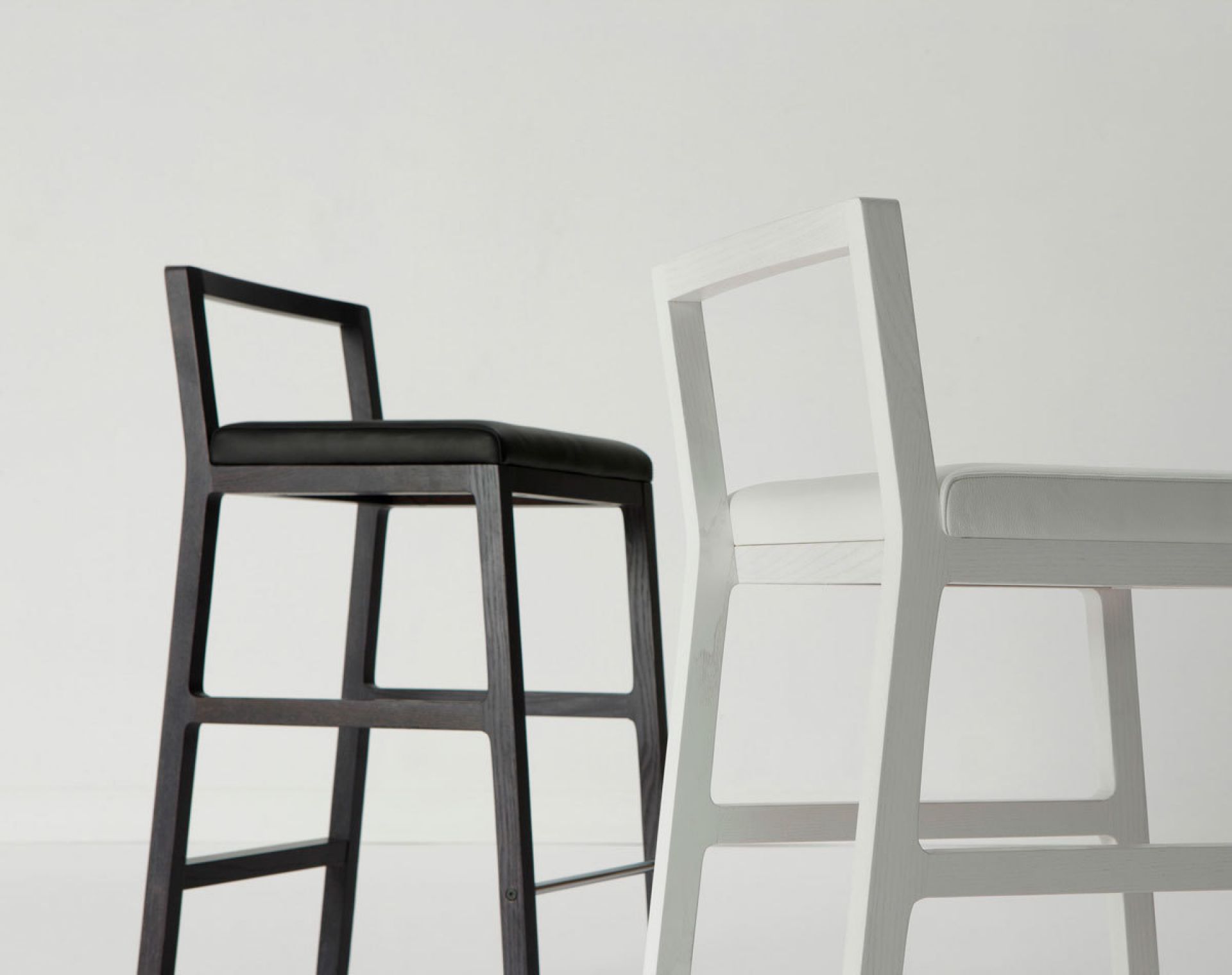 Midori Hocker Weiß von Sancal und ein schwarzer Hocker mit Sitzpolster vor weißem Hintergrund.