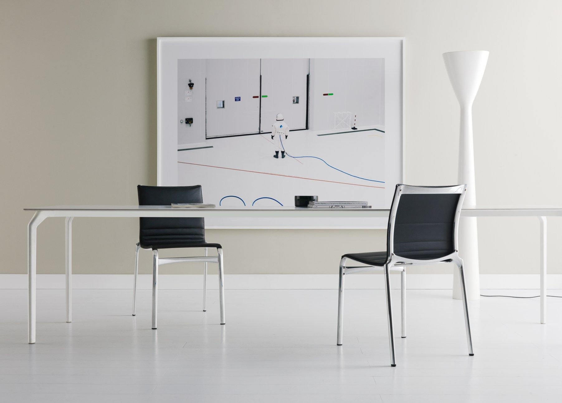 Tec Table Tisch Alias mit zwei schwarzen Stühlen und einem modernen Kunstwerk im Hintergrund.