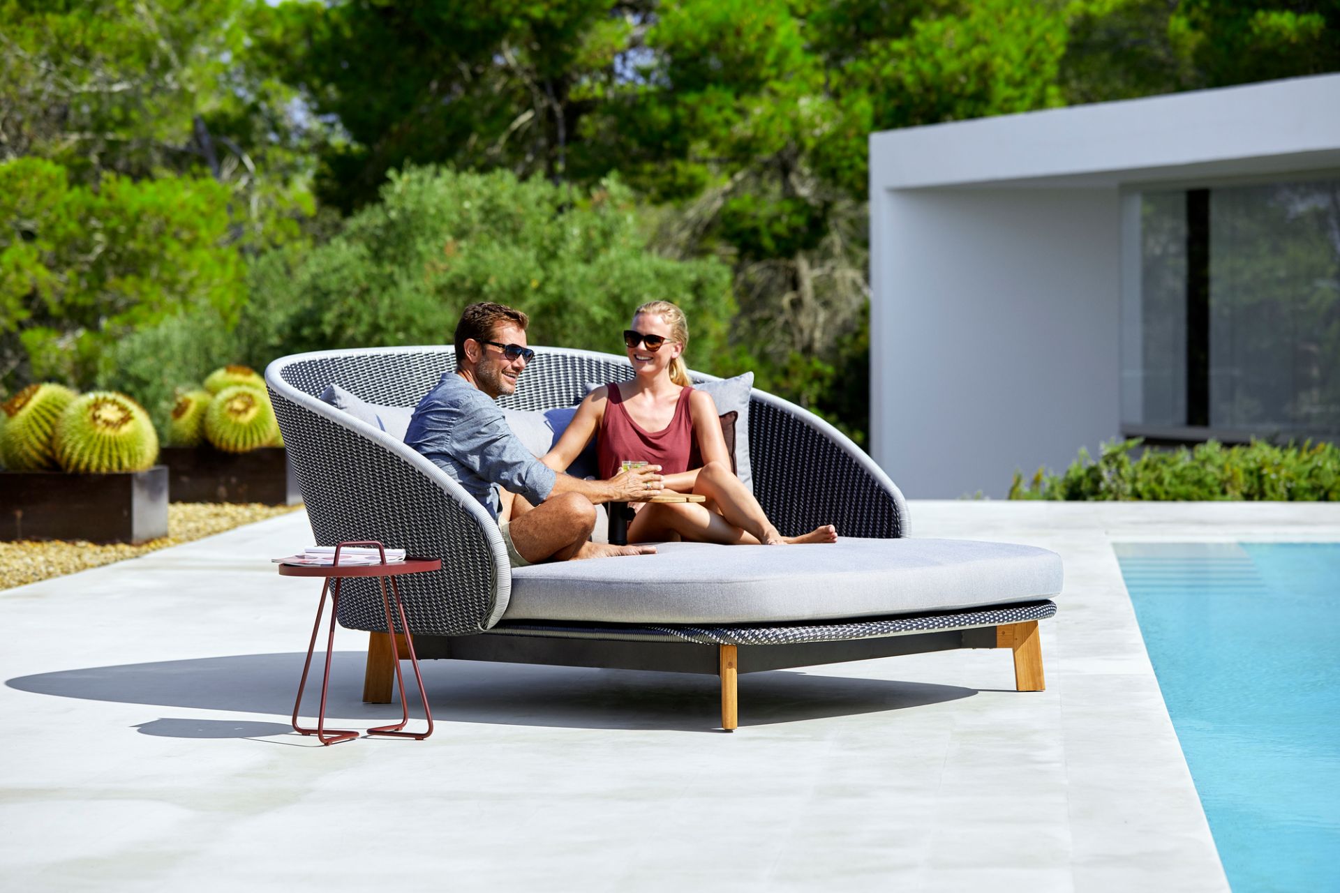 Paar entspannt auf Cane-Line Peacock Outdoor Liege mit Tisch und Kissen am Pool.