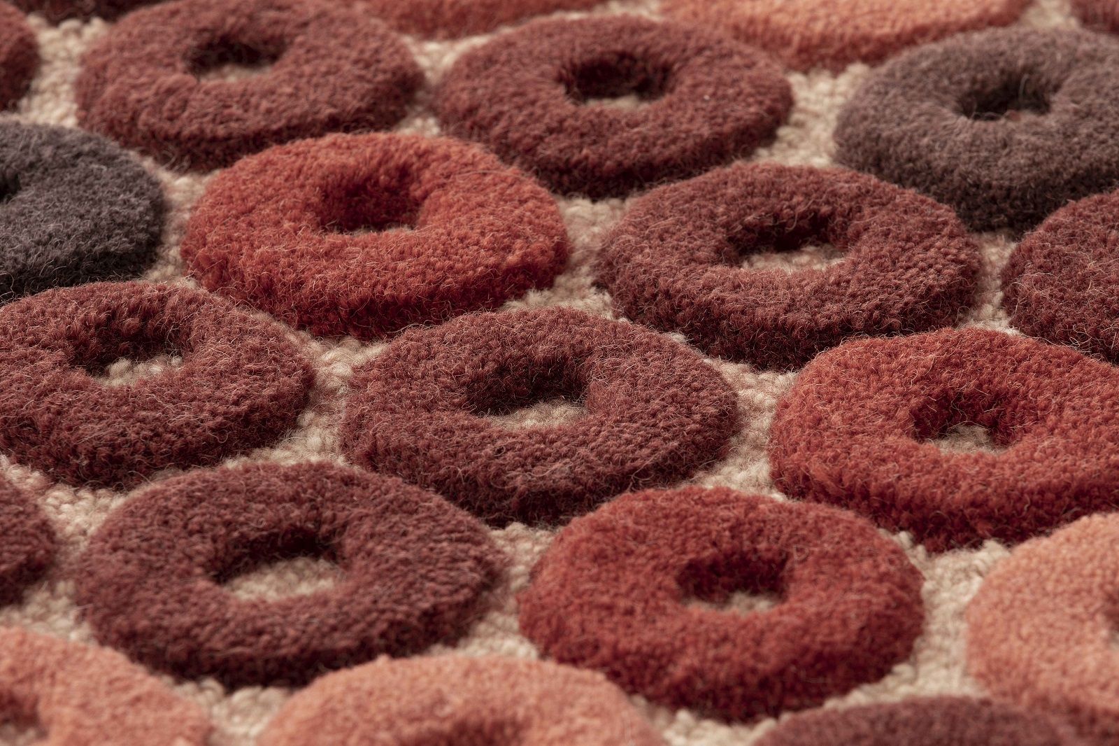 Detailaufnahme des Chimos Rug Teppichs mit braunen, ringförmigen Mustern auf beigem Grund. Hochwertiger Wollteppich.