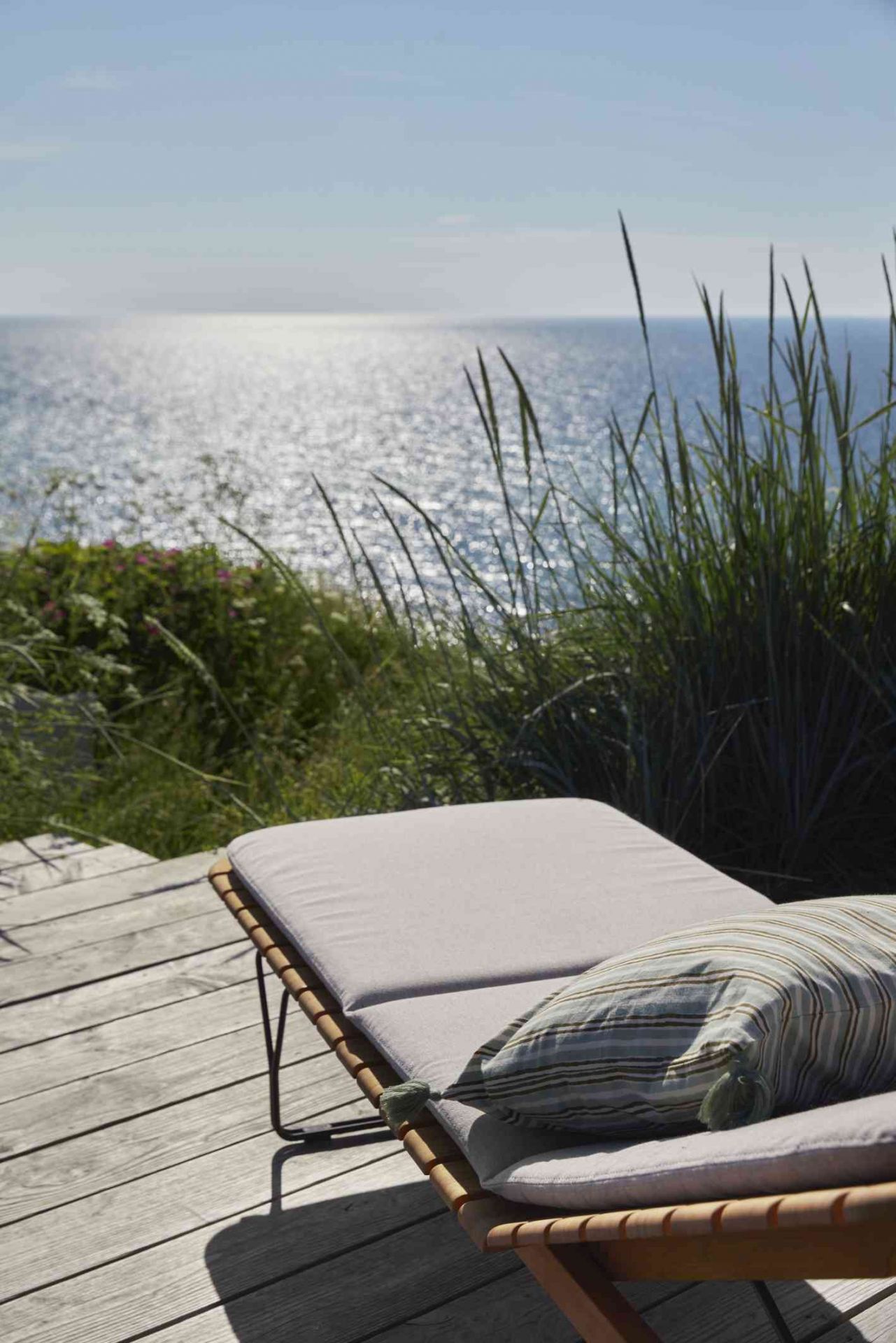 Molo Outdoor Cushion Kissen für Houe Sonnenliege auf Holzterrasse mit Meerblick. Gartenmöbel für Entspannung.