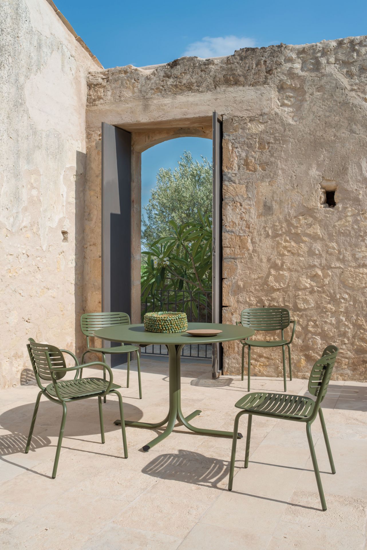 Grüne Emu Mom Armlehnstühle und Tisch auf einer Terrasse mit Steinmauer und blauem Himmel.