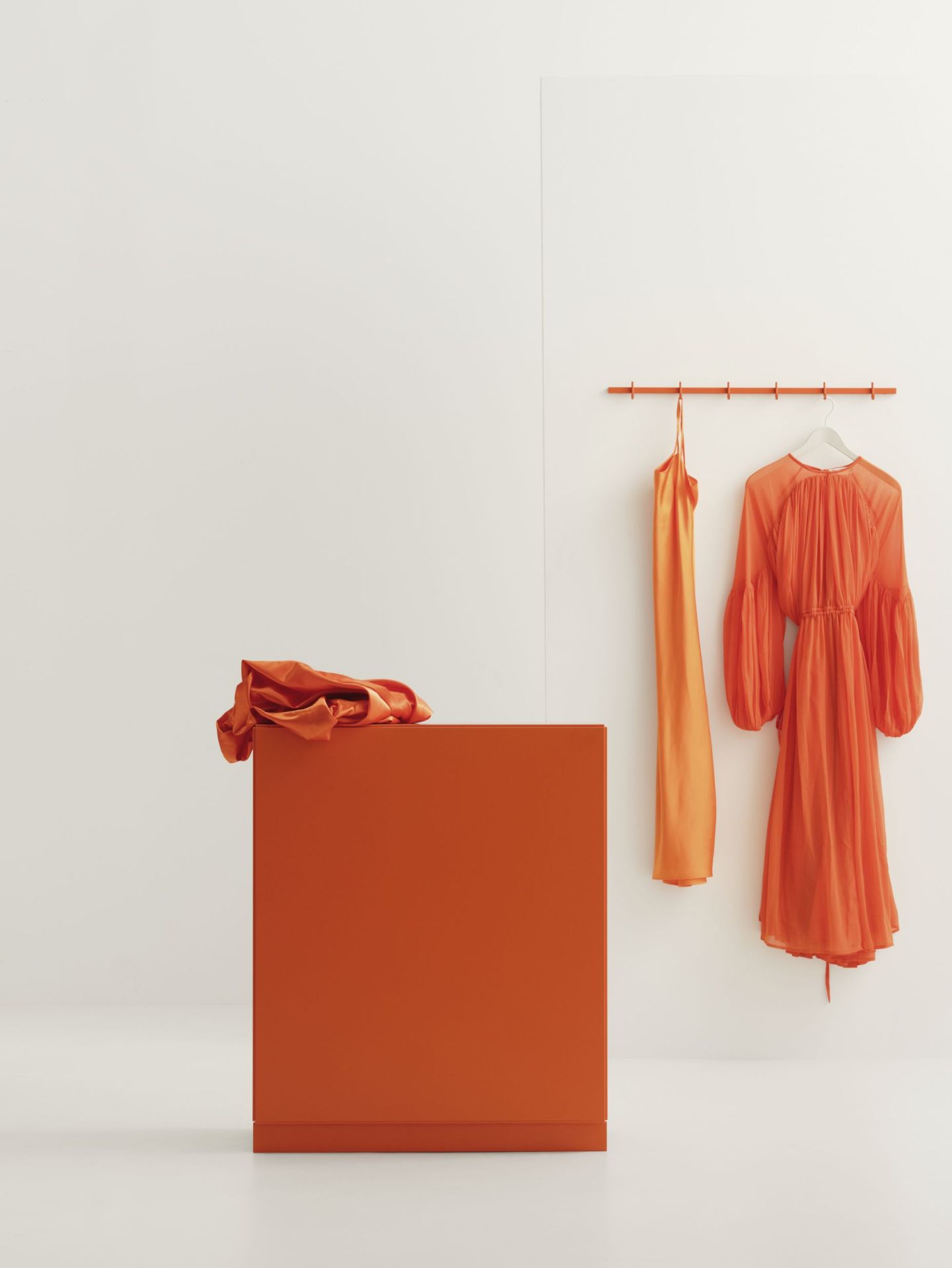 Orange Relief Kommode mit Sockel von String Furniture und zwei Kleidern an einer Kleiderstange.
