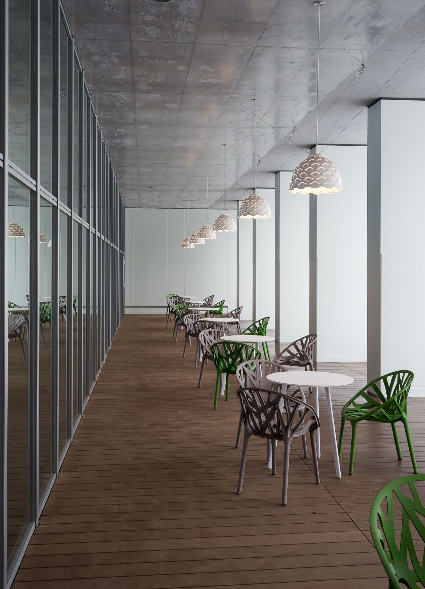 Reihe von LC Shutters Hängeleuchten von Louis Poulsen über Tischen und Stühlen in einem Raum.