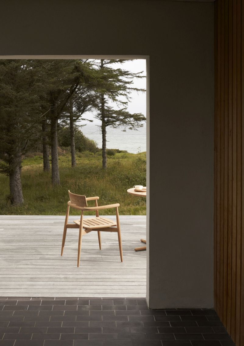 E008 Embrace Stuhl von Carl Hansen & Søn auf Holzterrasse mit Meerblick. Outdoor-Stuhl aus Holz.
