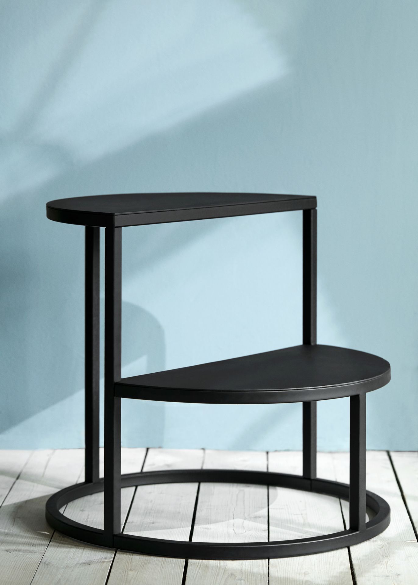 Schwarzer Dais Stufenhocker mit zwei Ablageflächen und Metallgestell auf hellem Holzboden. Dekorative Trittstufe.