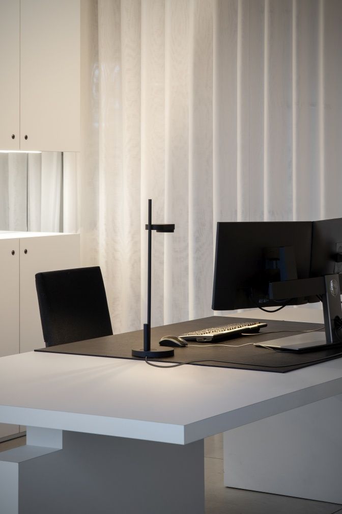 Schwarze Kido Tischleuchte von Belux mit Rundfuss auf einem weißen Schreibtisch.