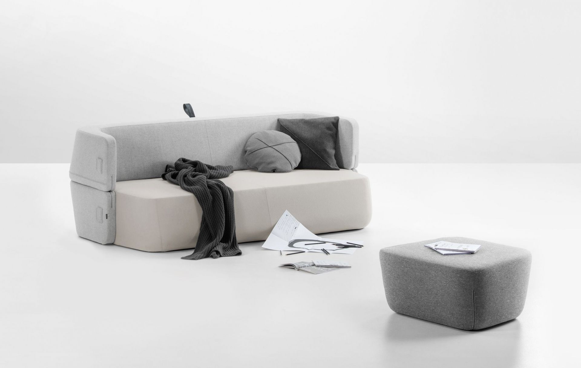 Graues Revolve Schlafsofa von Prostoria mit Kissen und Hocker auf weißem Hintergrund.