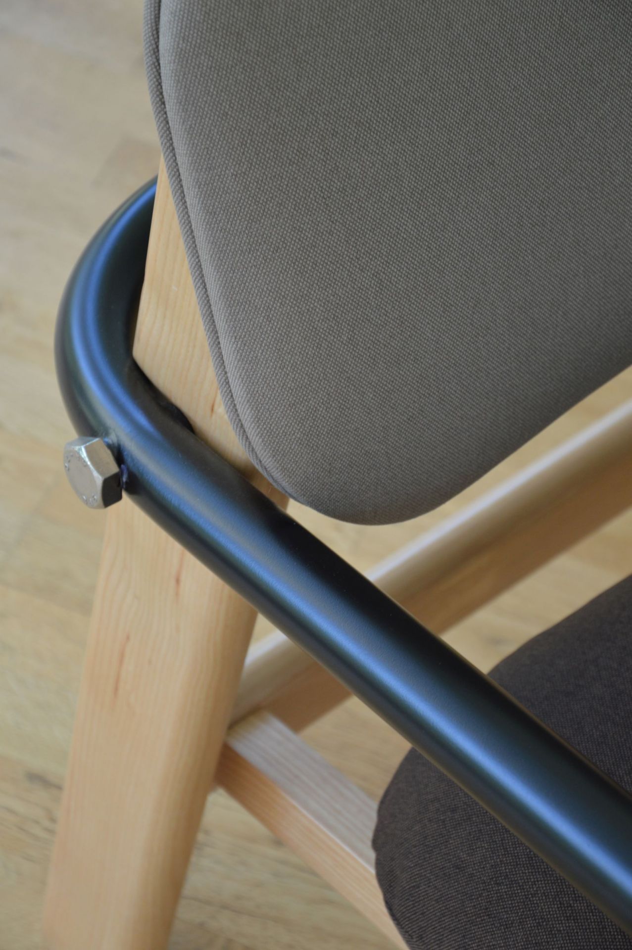 Detailaufnahme des Billy Stuhls von Jan Kurtz: Grauer Stoffbezug, Holzgestell und schwarze Armlehne.