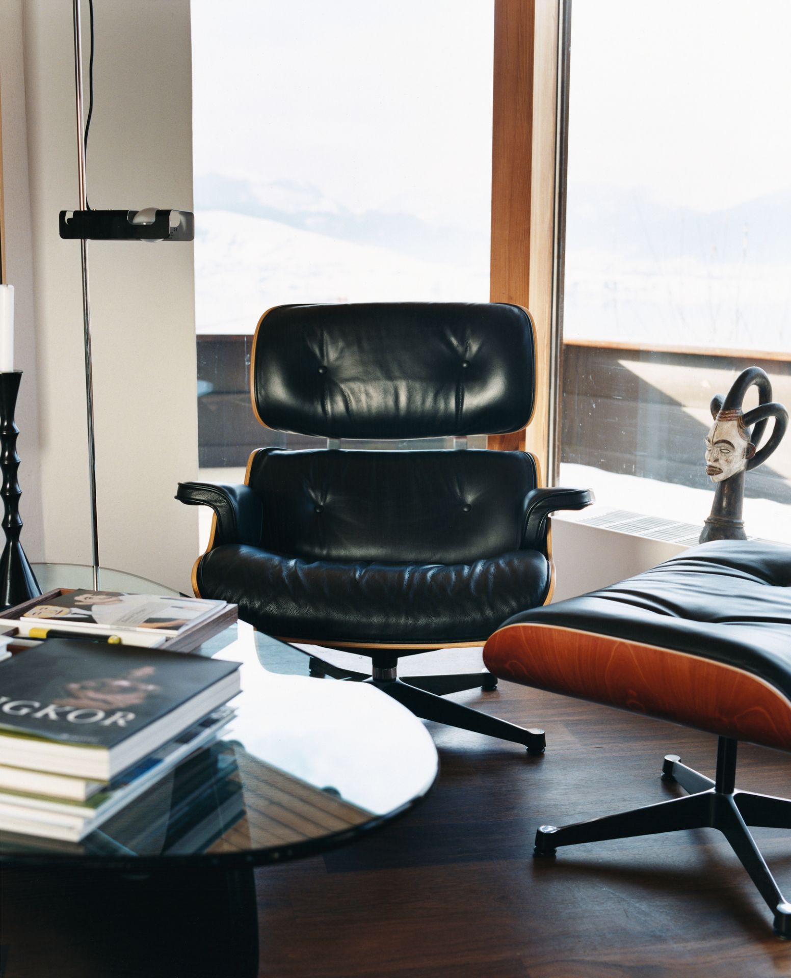 Nussbaum Couchtisch mit Glasplatte, Bücherstapel und schwarzem Ledersessel im modernen Wohnzimmer.