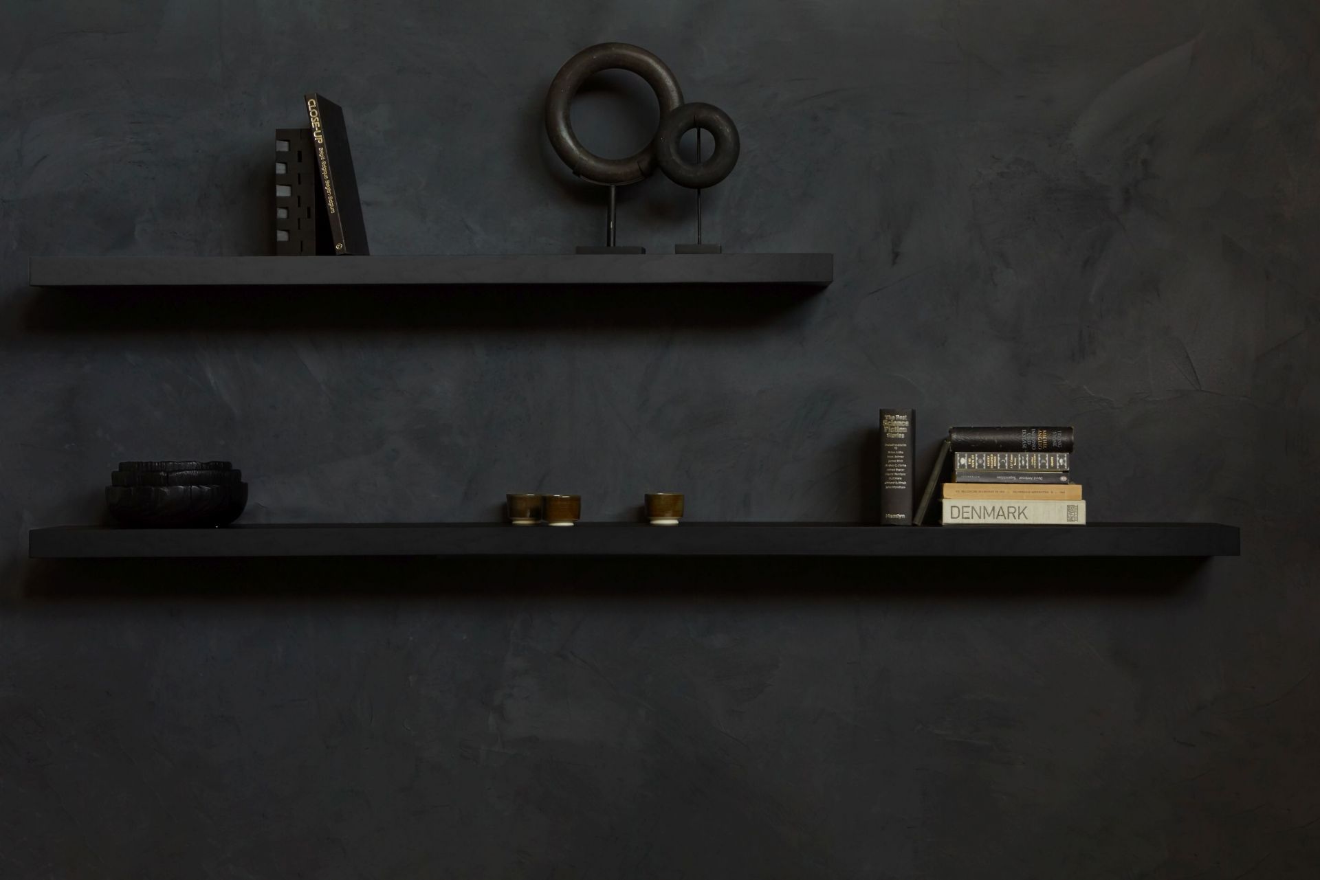 Schwarzes Ethnicraft Wandregal aus Eiche, lackiert, mit Deko-Objekten und Büchern vor einer dunklen Wand.