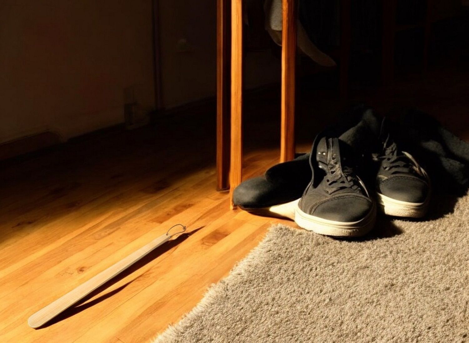 Helping Friend Schuhlöffel lang aus Holz neben Schuhen auf Teppich und Parkettboden.