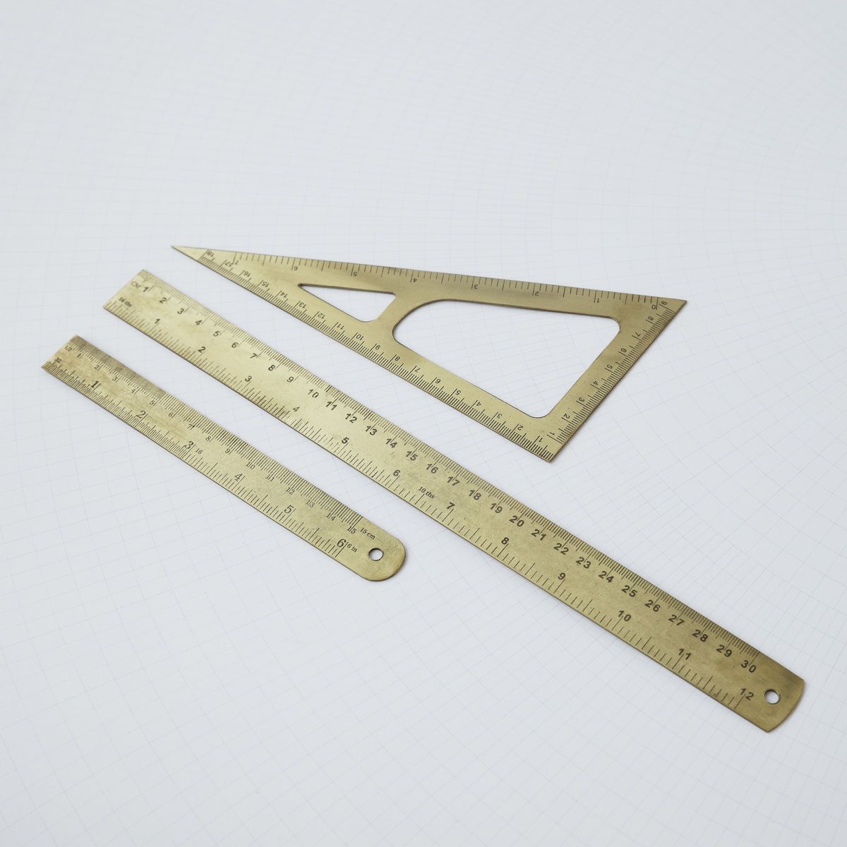 Goldfarbenes Lineal-Set mit 15 cm Lineal, Geodreieck und kurzem Lineal auf kariertem Hintergrund.