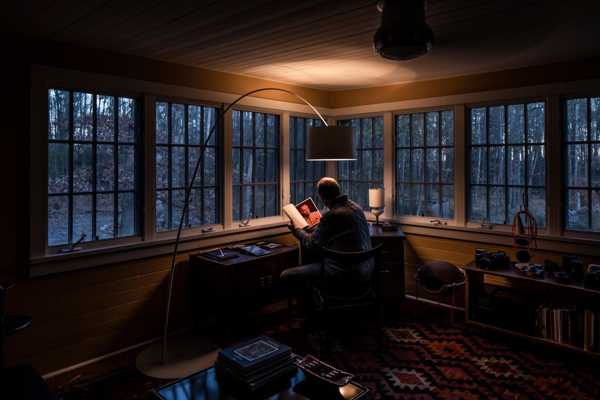 Mann liest unter der grauen Foscarini Twiggy Stehleuchte in gemütlichem Wohnzimmer mit Blick auf den Wald.