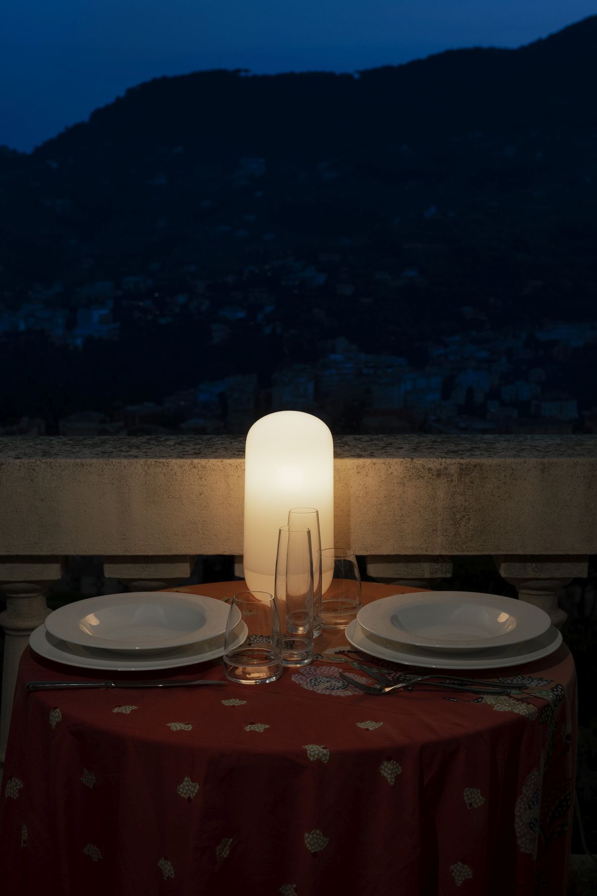 Gedeckter Tisch mit der Gople Portable Akkuleuchte von Artemide im Hintergrund. Tischleuchte für stimmungsvolles Licht.