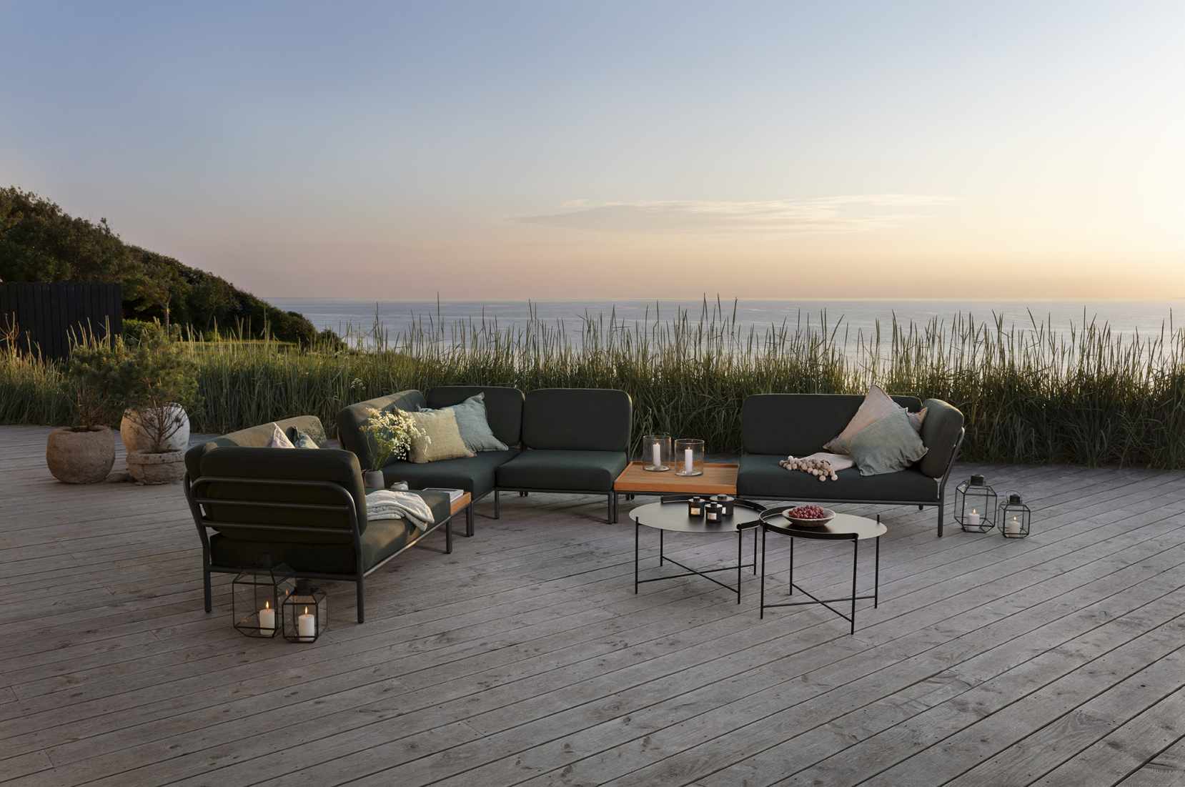 Houe Level Outdoor Sofa Ecke links auf Holzterrasse mit Meerblick, Gartenmöbel und Dekoration.