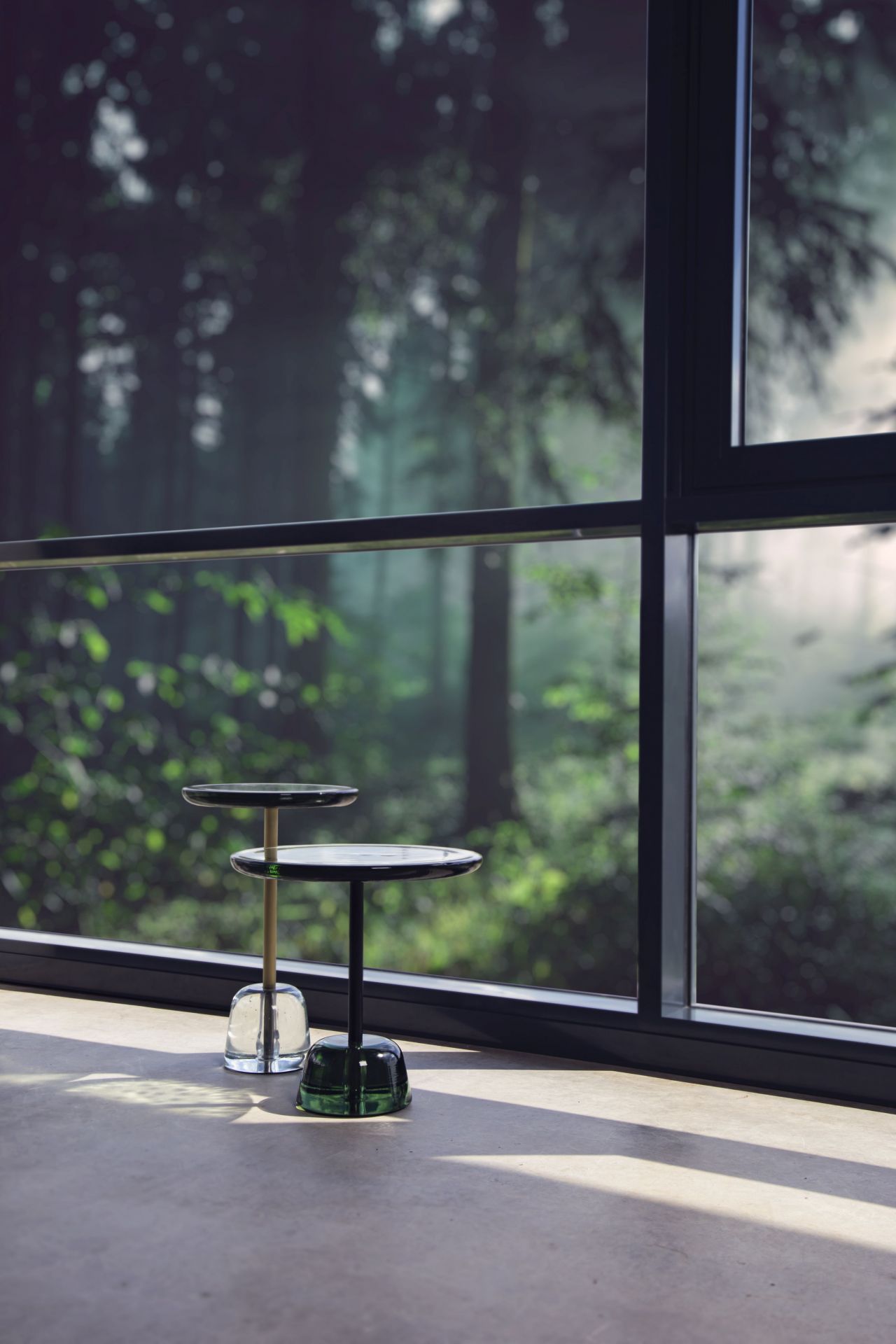 Zwei Pina High Beistelltische von Pulpo aus Glas und Metall vor Fenster.