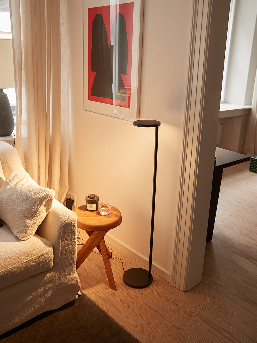 Moderne, braune Flos Stehleuchte Oblique in mattem Finish neben Sofa und Beistelltisch.