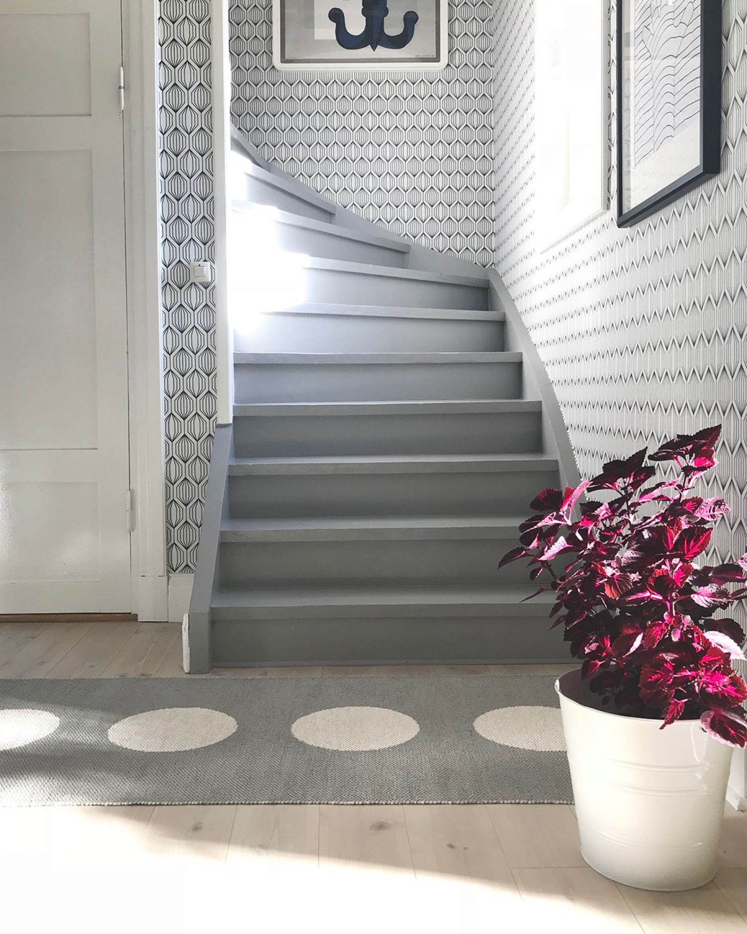 Grauer Vera Kunststoffteppich von Pappelina im Flur vor einer Treppe mit weiß gepunktetem Muster.