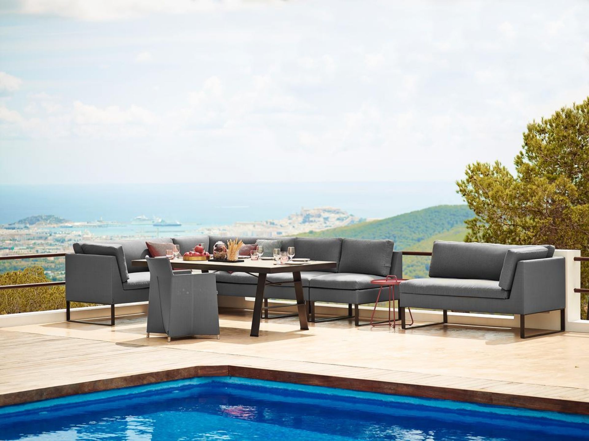 Graues Cane-Line Outdoor Sofa 2-Sitzer rechts auf Terrasse mit Pool und Meerblick. Gartenmöbel.