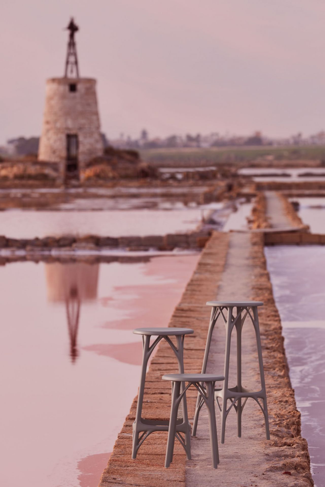 Drei graue A.I. Hocker von Kartell auf einem Steg vor einem Turm. Design Hocker.