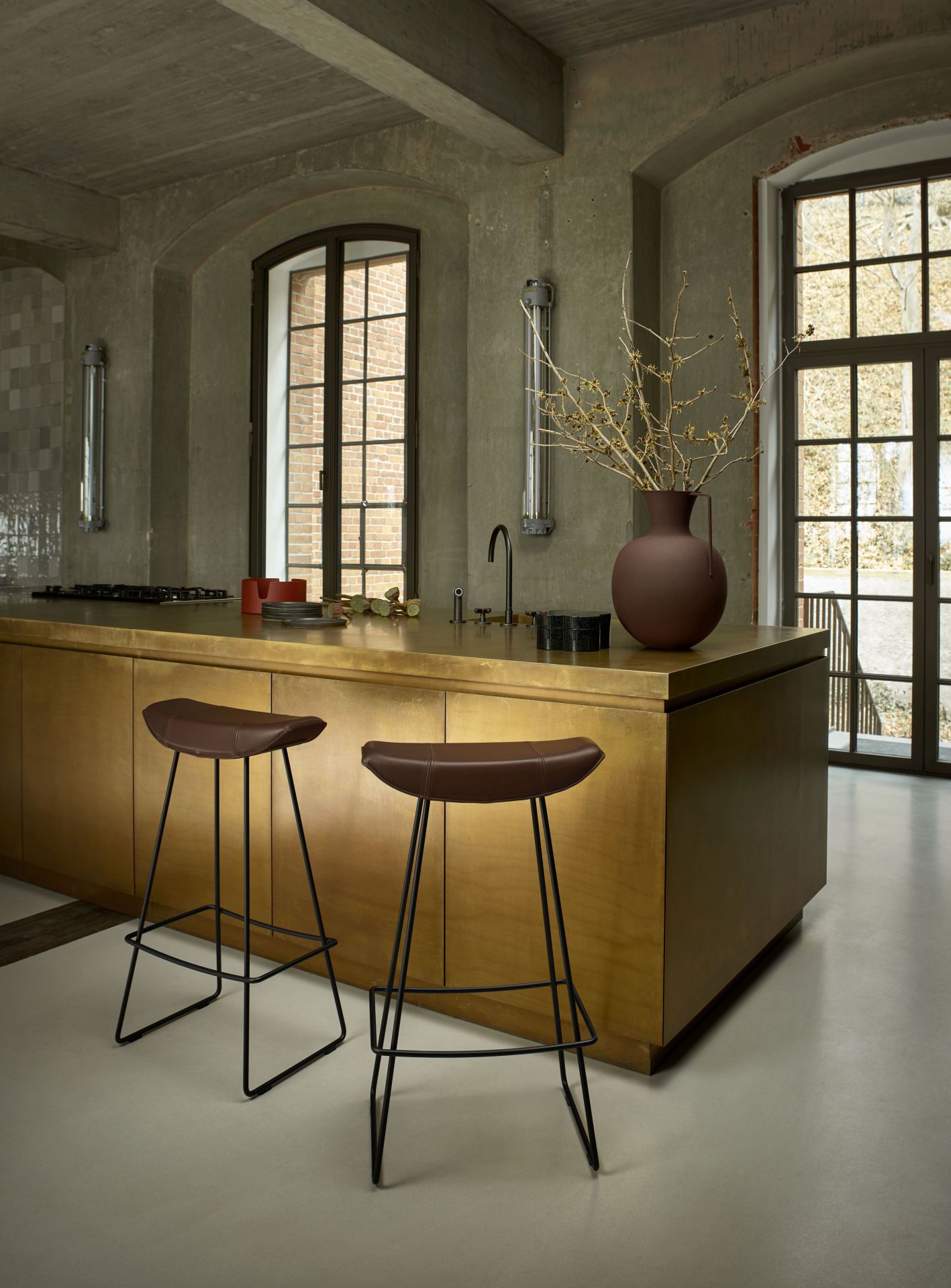 Zwei braune Kya Barhocker von Freifrau Manufaktur vor einer Kücheninsel in Loft-Atmosphäre.