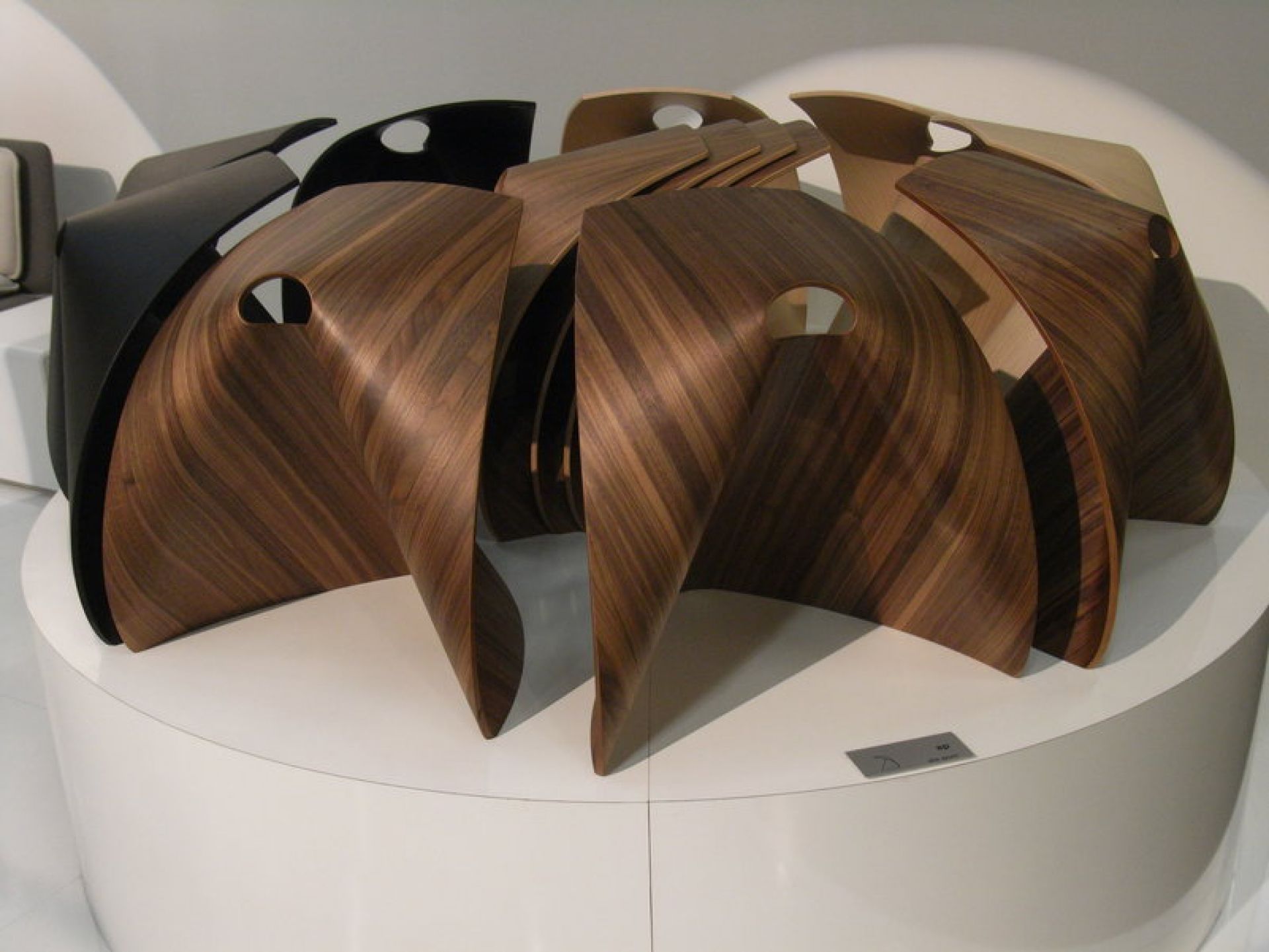 Mehrere La Palma Hocker AP aus Holz in verschiedenen Farben auf einem Podest.