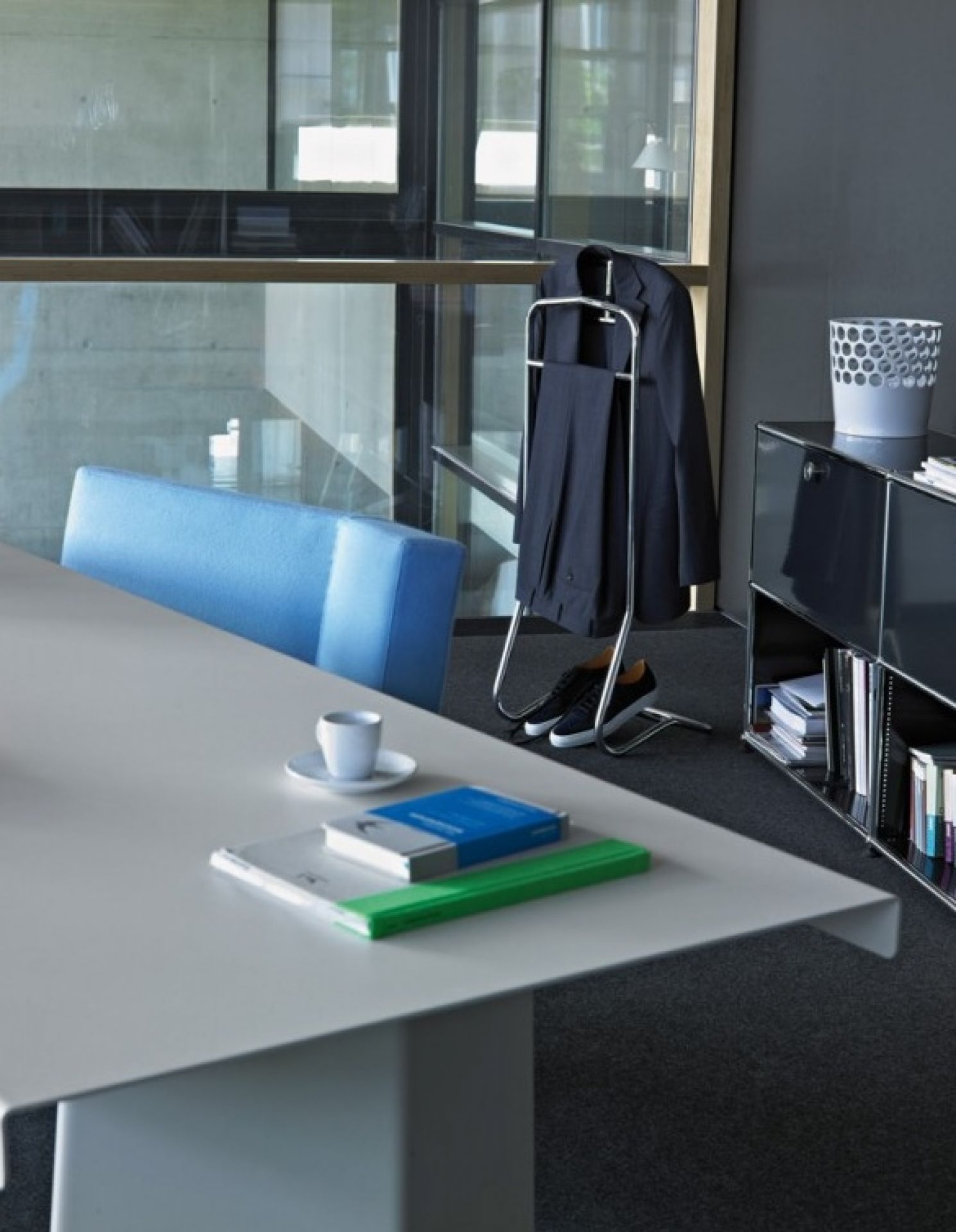 Detailaufnahme eines ClassiCon Tisches mit Kaffeetasse, Büchern und Kleiderständer in einem modernen Büro.