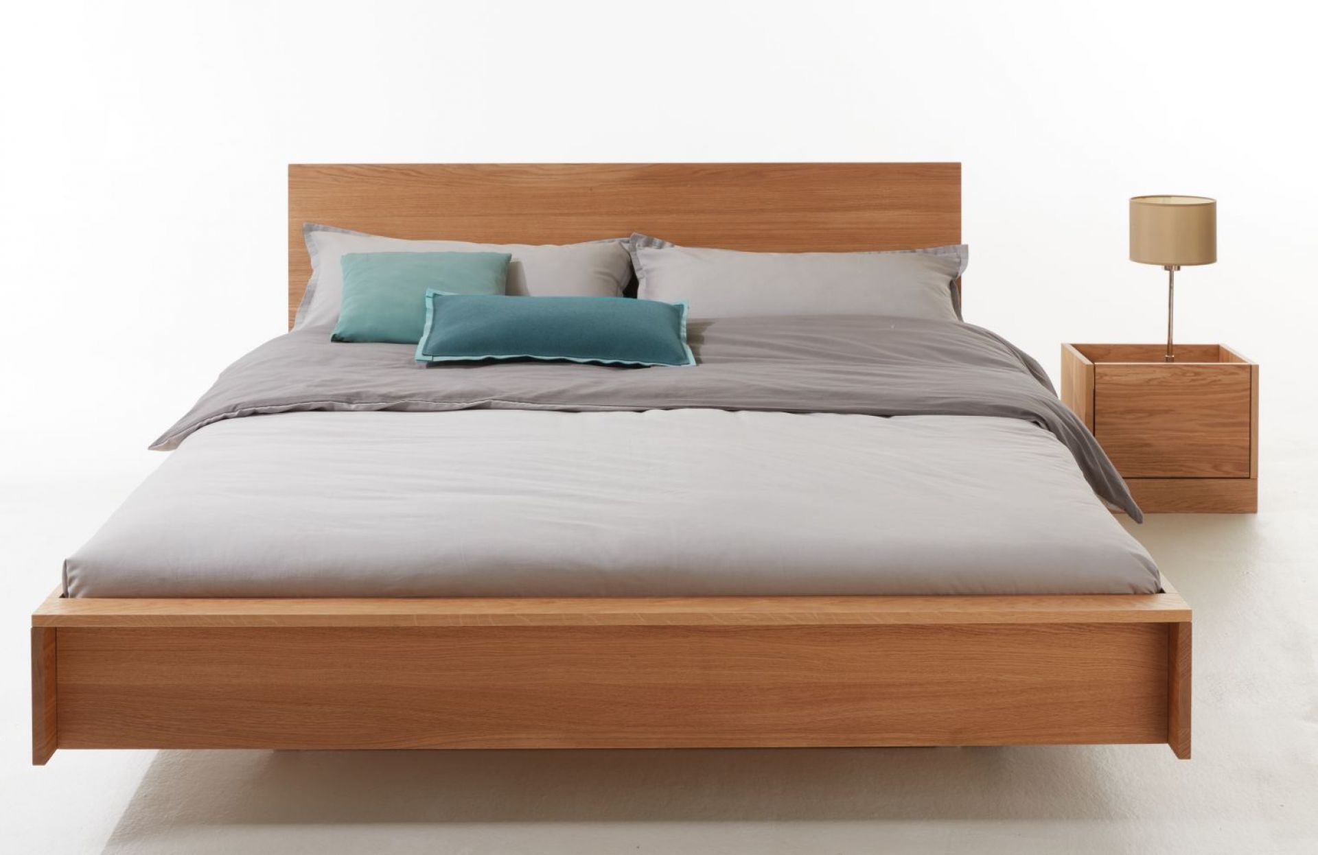 Bett mit Kopfteil aus Eiche, passender Nachttisch und Textilien in Grau und Türkis.