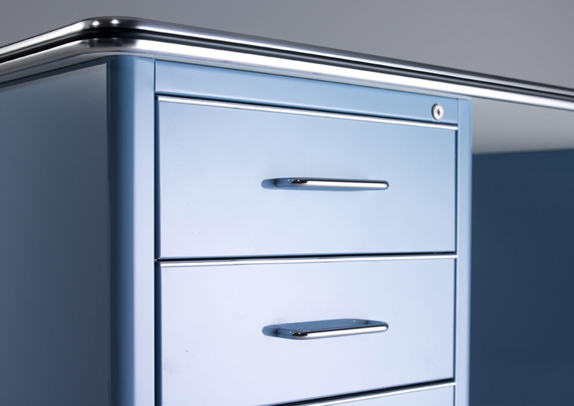 Detailaufnahme des blauen Müller Möbelfabrikation TB 225 Classic Line Schreibtischs mit drei Schubladen und Chromgriffen.