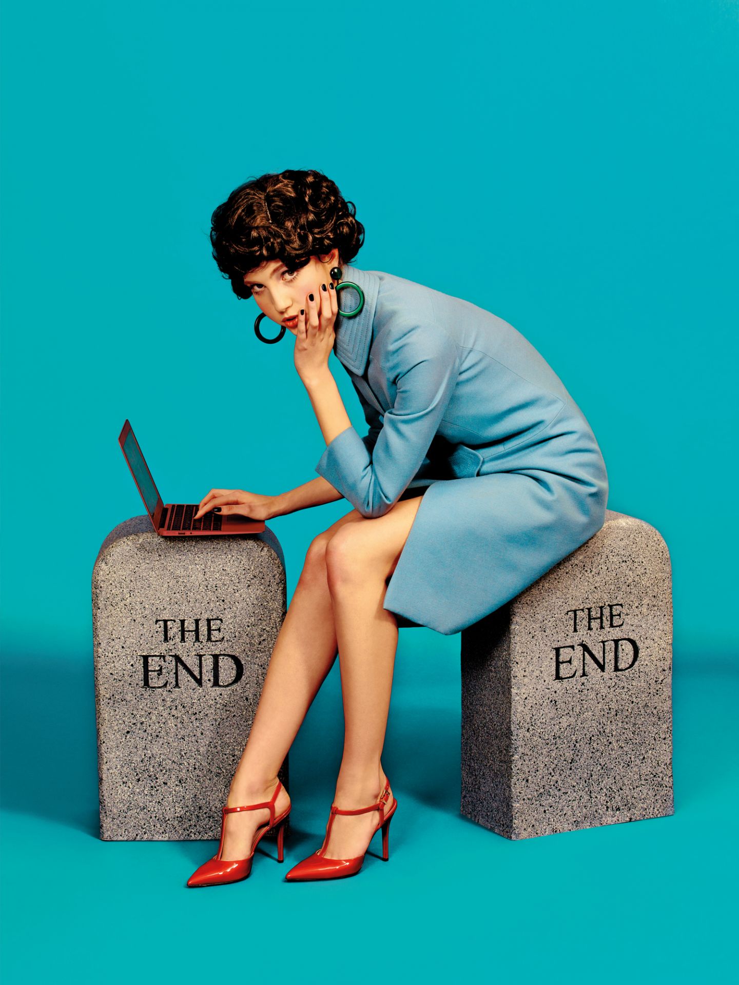 Frau sitzt auf zwei grauen "The End" Hockern von Gufram und tippt auf einem Laptop.