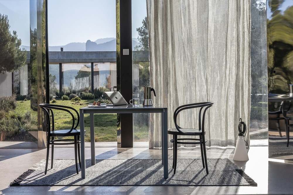 Moderner Wohnraum mit grauem Nanimarquina Teppich, Tisch und Stühlen vor Panoramafenster.