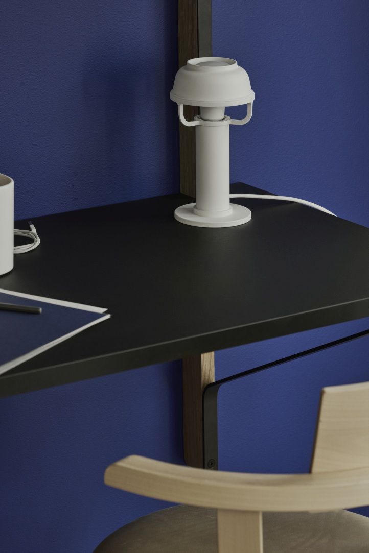 Nahaufnahme der weißen Kori Table Light Tischleuchte von Artek auf einem schwarzen Schreibtisch.