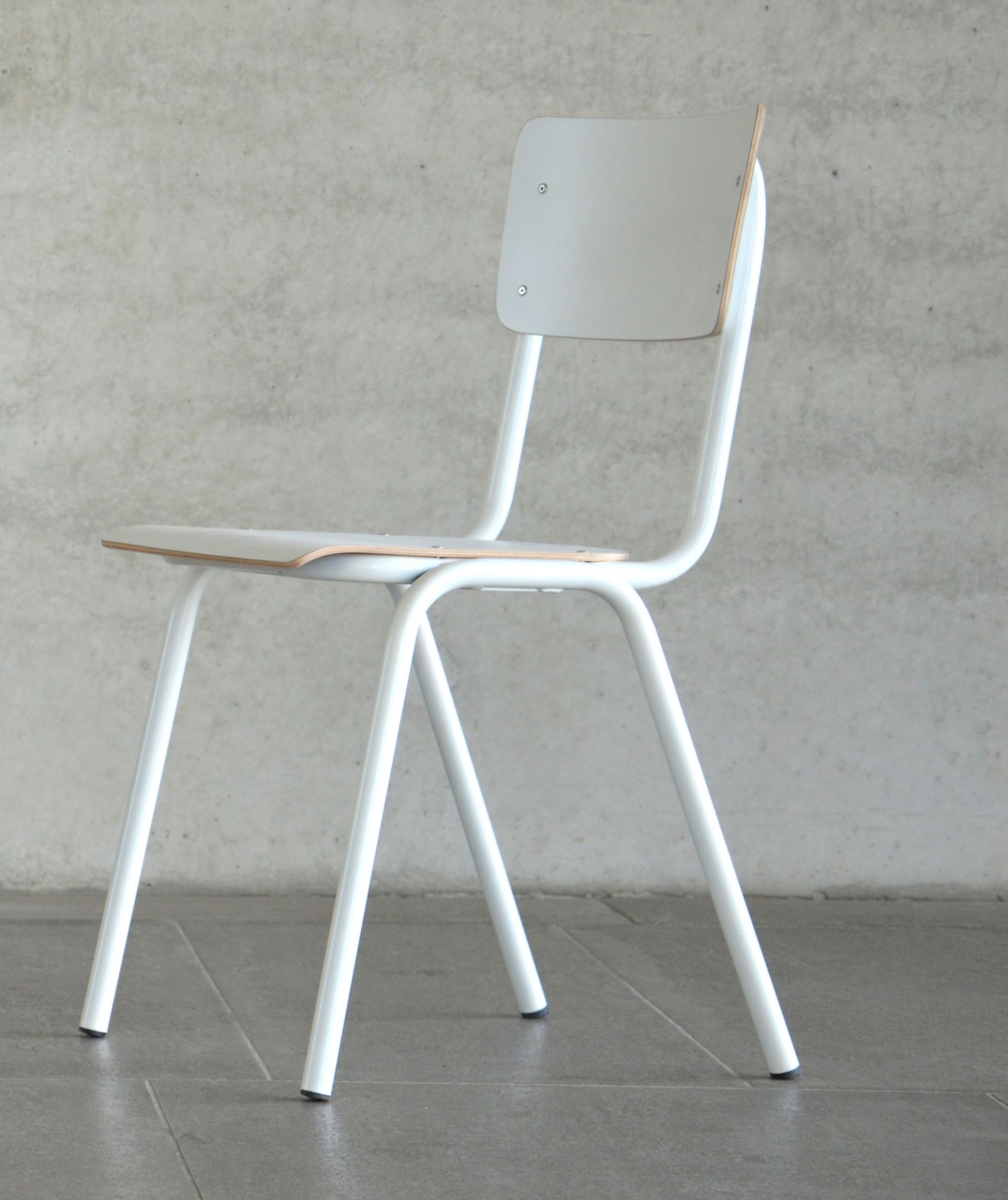 Weißer Zero Stuhl von Jan Kurtz mit minimalistischem Design und Stahlrohrgestell vor Betonwand.