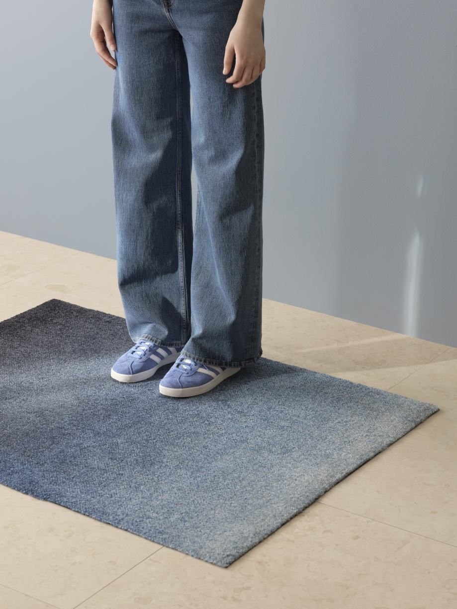 Person mit blauen Schuhen steht auf der blauen Dis Fußmatte von Heymat für Innen und Außen.