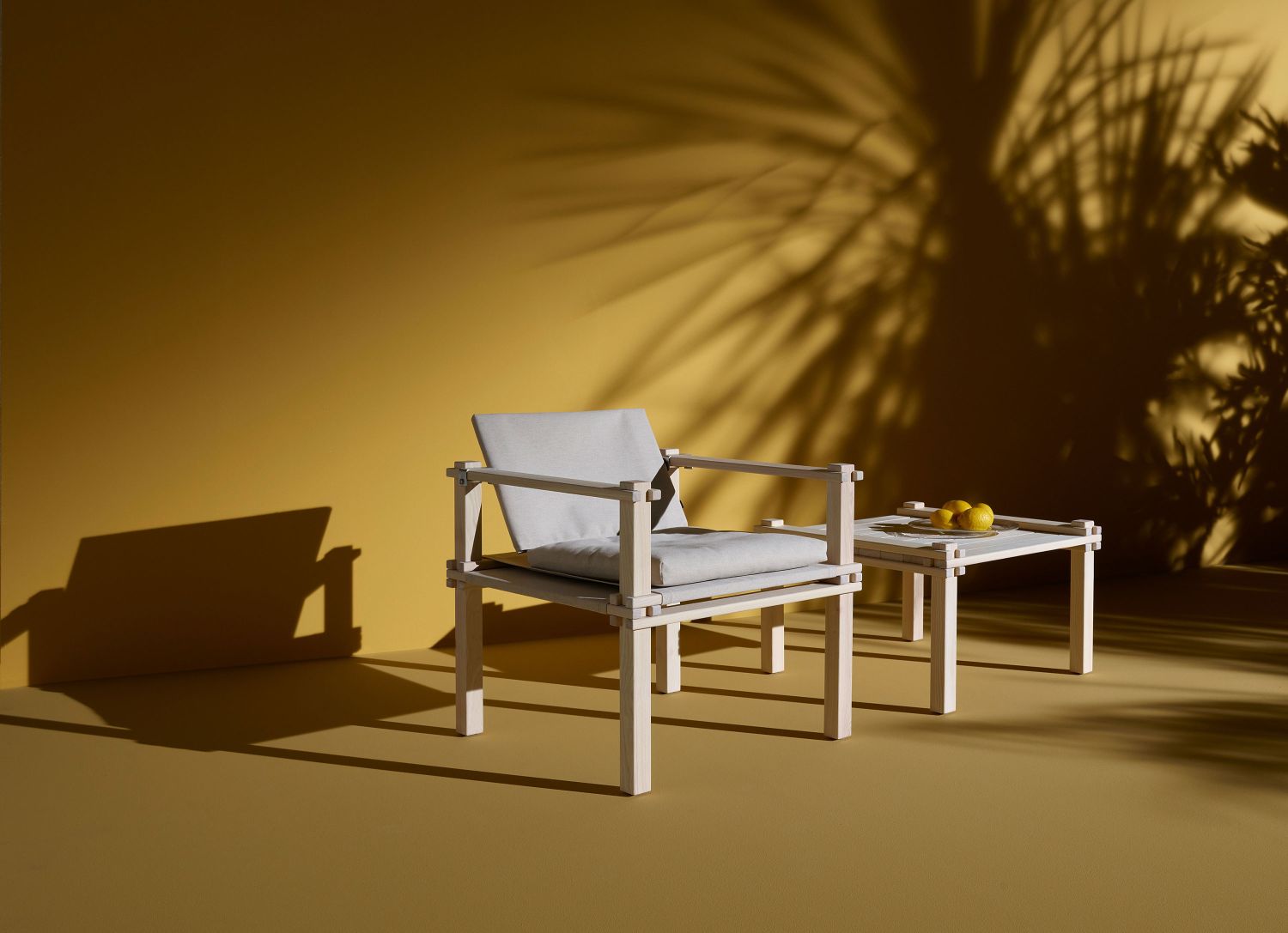 Farmer Outdoor Tisch und Stuhl aus hellem Holz mit Kissen vor gelbem Hintergrund.