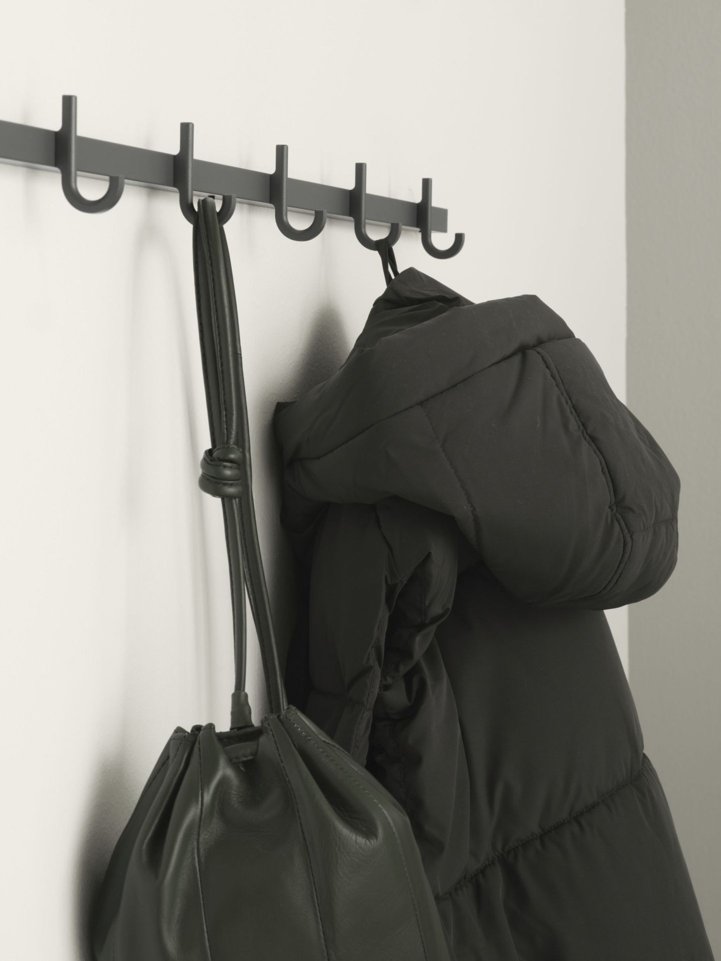 Weiße Relief Hakenleiste von String Furniture mit Jacke und Tasche. Wandgarderobe für Flur und Eingangsbereich.